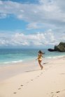 Счастливая взволнованная женщина в желтом бикини гуляет по песчаному пляжу у океана — стоковое фото