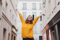 Smiling woman in yellow cardigan standing on street with hands up — Stock Photo