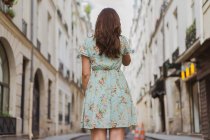 Vue arrière de la jeune femme en robe florale à motifs debout sur la rue — Photo de stock