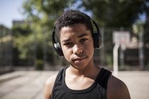 Afro jeune garçon écoute de la musique avec écouteurs sur le terrain de basket — Photo de stock