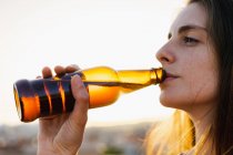 Счастливая молодая женщина пьет пиво из бутылки на открытом воздухе — стоковое фото