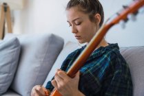 Young woman playing guitar on sofa — Stock Photo