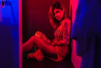 Приваблива молода жінка в одязі, сидячи на підлозі в туалеті з яскраво-червоним освітленням — стокове фото