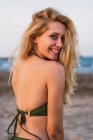 Femme gaie en bikini assis sur la plage et regardant la caméra — Photo de stock
