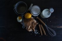 Сельский укладка риса, молока, специй и лимонов на черном деревянном столе с посудой — стоковое фото
