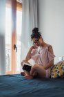 Brünette Frau mit Buch sitzt auf dem Bett und schaut in die Kamera — Stockfoto