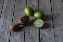 Fresh whole and halved limes with wooden squeezer on grey wood — Stock Photo