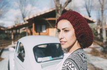 Young woman in wool hat standing in front of old car and looking away — Stock Photo