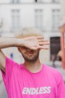 Модный бородатый мужчина в розовой футболке стоит на улице на фоне размытости — стоковое фото