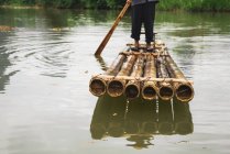 Primer plano del aldeano de pie en balsa de bambú en el río - foto de stock