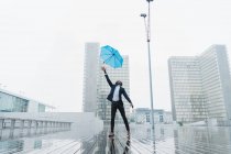 Ethnic businessman catching umbrella while standing on wet pavement in city — Stock Photo