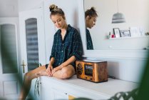 Young woman in oversize checkered shirt sitting on counter near retro radio receiver — Stock Photo