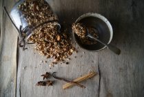 Перевернутая банка вкусной мюсли с приправами чая на деревянном столе с миской и различными ароматами — стоковое фото