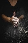 Menschenhände schütteln Mehl und Teigstücke auf schwarzem Hintergrund ab — Stockfoto