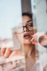 Alluring woman with eyeglasses looking at camera behind window — Stock Photo