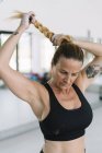 Starke blonde Frau in Sport-BH macht Zopf während des Trainings im Fitnessstudio — Stockfoto