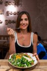 Усміхнена жінка сидить у кафе з мискою їжі і дивиться на камеру — стокове фото