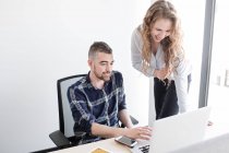 Donna e uomo sorridenti alla scrivania dell'ufficio che guardano il computer portatile insieme e lavorano in squadra all'interno dell'ufficio moderno — Foto stock