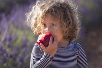 Kleines Mädchen isst im Sonnenlicht Pfirsich auf der Wiese — Stockfoto