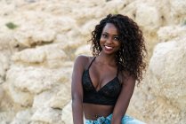 Charming black woman in lace top looking at camera against cliff — Stock Photo