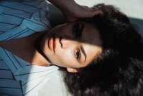 Jovem mulher morena pensativa com cabelos longos deitado no chão na sombra e luz solar — Fotografia de Stock
