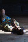 Femme tatouée sensuelle couché avec les yeux fermés sur le sol — Photo de stock
