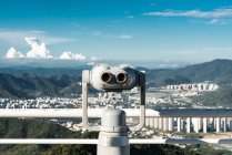 Construção branca de visualizador binocular de moedas no terraço contra a paisagem urbana em montanhas tropicais, Phoenix Park, China — Fotografia de Stock