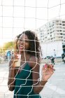 Fröhliche schwarze Frau mit Getränk steht hinter Netz am Strand — Stockfoto
