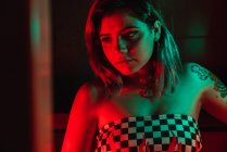 Молода жінка дивиться геть, стоячи в кімнаті з червоним і зеленим освітленням — стокове фото
