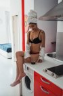 Femme sensuelle en lingerie avec serviette sur les cheveux assis sur le comptoir avec tasse de café — Photo de stock