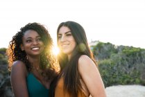 Разнообразные молодые женщины стоят и улыбаются на фоне природы в задней освещении — стоковое фото
