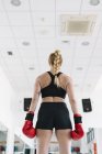 Rückenansicht einer muskulösen Frau in roten Boxhandschuhen, die im Fitnessstudio steht — Stockfoto