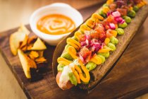 Close-up of delicious hot dog garnished with vegetables and sauce on wooden board — Stock Photo