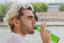 Blond bearded male holding cigarette in hand while drinking beer on street on blurred background — Stock Photo
