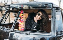 Portrait de jeune femme en manteau noir et lunettes de soleil assis à l'intérieur de la voiture — Photo de stock