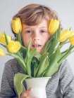Молодий хлопчик з жовтими тюльпанами в глечику дивиться на камеру — стокове фото