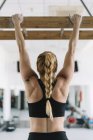 Back view of strong woman in sportswear hanging on wooden board in gym and pulling up — Stock Photo