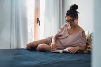 Focused brunette woman reading book on bed — Stock Photo