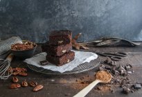 Pieces of delicious chocolate brownie o n wire rack with ingredients on dark wooden surface — Stock Photo