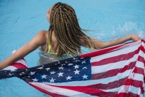 Visão traseira da mulher em pé na piscina segurando bandeira americana — Fotografia de Stock