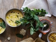 Sopa de crema de maíz con coco y pesto en tazón sobre mesa de madera con ingredientes - foto de stock