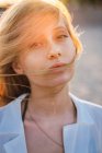 Blond young woman with blowing hair standing in sunlight and looking at camera — Stock Photo