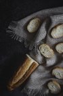Partly sliced baguette on sackcloth on black surface — Stock Photo