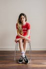 Young woman in red outfit sitting on chair and looking at camera — Stock Photo