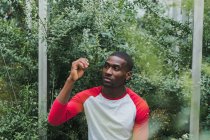 Junger schwarzer Mann sitzt zwischen grünen Büschen im Gewächshaus — Stockfoto
