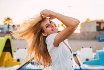 Fröhliche blonde Frau, die am Strand steht und Haare berührt — Stockfoto