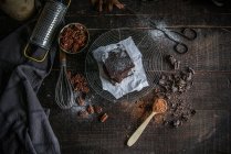 Pezzi di delizioso brownie cioccolato o n rack filo con ingredienti su superficie di legno scuro — Foto stock