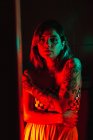 Sinnliche junge Frau mit Tätowierungen blickt in dunklen Raum in die Kamera — Stockfoto