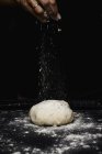 Human hand powdering bread with flour on kitchen table on black background — Stock Photo