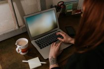 Крупним планом татуйована жінка друкує на ноутбуці і тримає смартфон за старовинним столом — стокове фото